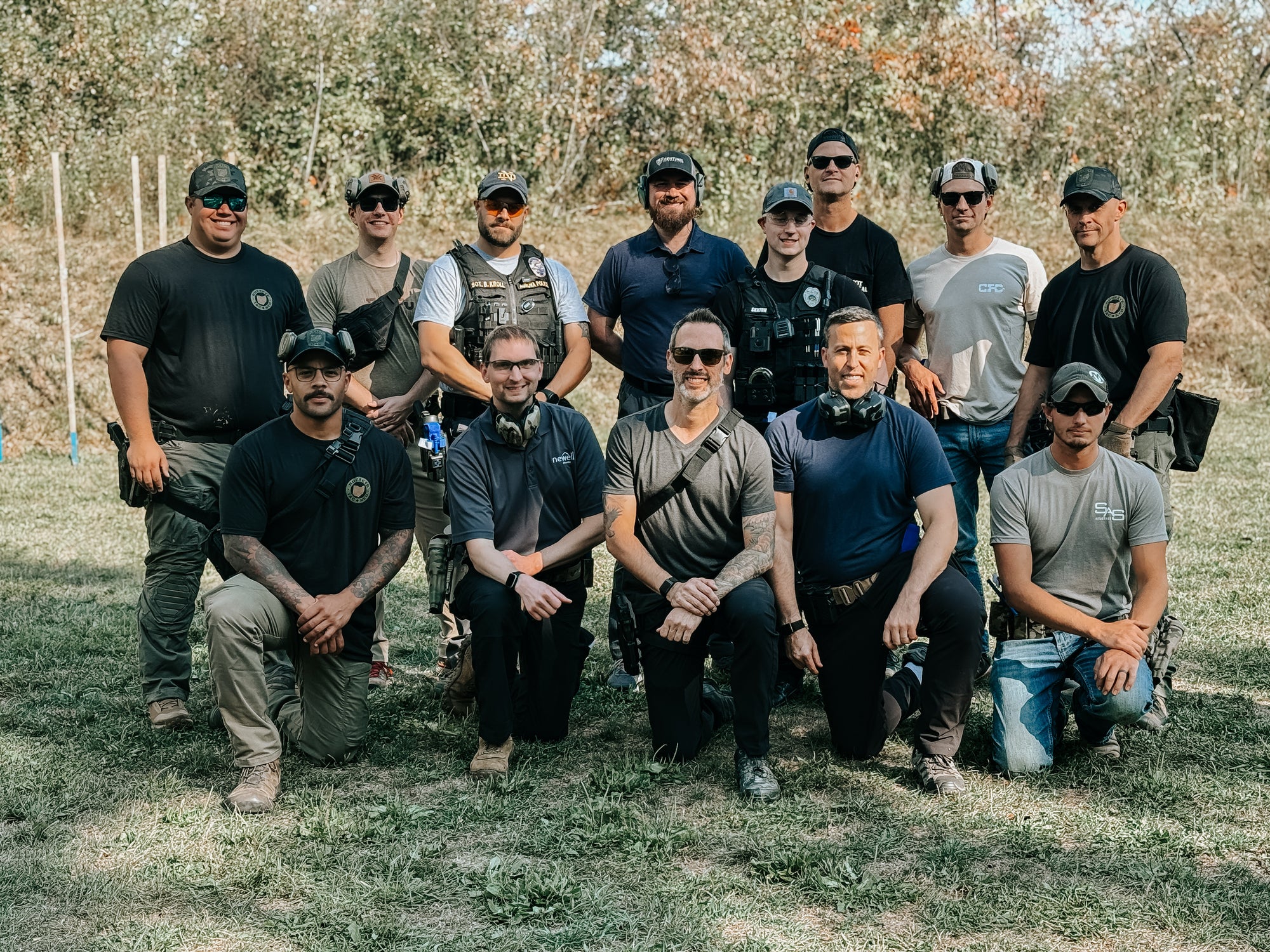 Group of men in tactical gear posing outdoors with trees in the background